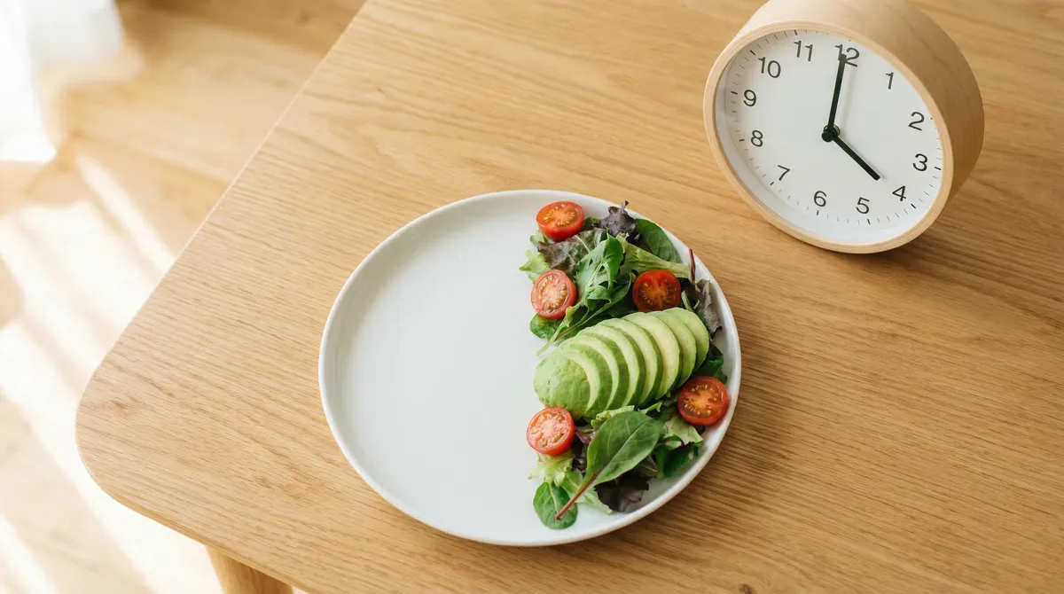 Assiette à moitié remplie de légumes frais à côté d'une horloge symbolisant la fenêtre de jeûne intermittent
